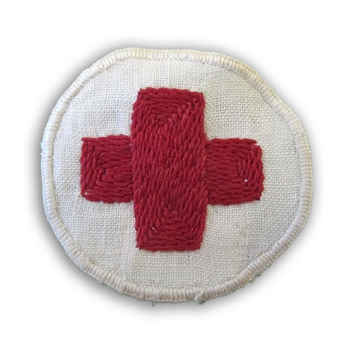 Lottamerkit kuvailtuna: Lääkintälottien valkoinen kangasmerkki, jossa punainen risti keskellä