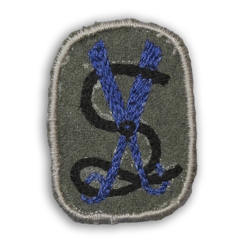 Lottamerkit kuvailtuna: Varuslottien kankainen merkki, jossa siniset sakset ja mittanauha harmaalla pohjalla