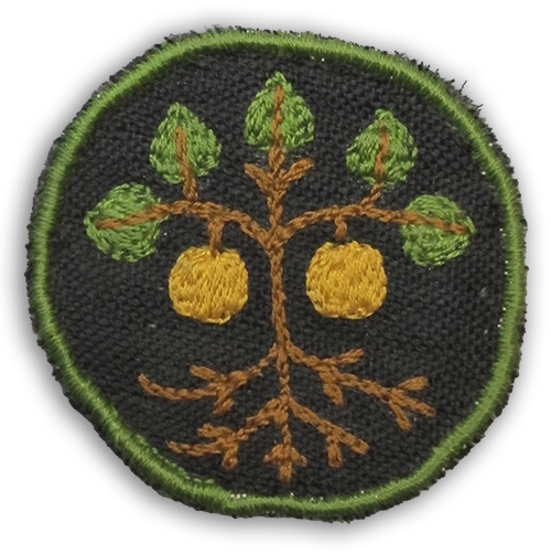 Huoltolottien kankainen merkki, jossa mustalla pohjalla ruskea puu, viisi vihreää lehteä, ja kaksi keltaista hedelmää