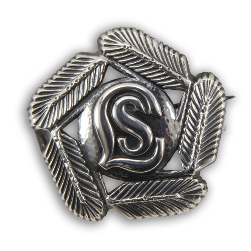 Lottien hopeinen hiihto- ja kävelymerkki, jossa havukoristelu reunoilla ja keskellä kirjaimet LS