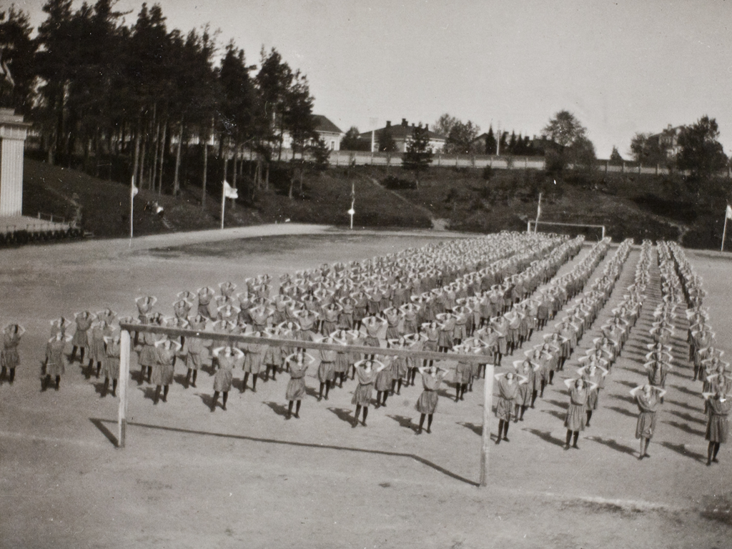 Lottavoimistelijoiden asuun kuului näytöksissä hame, sandaalimalliset kengät ja toisinaan myös tummat sukat.