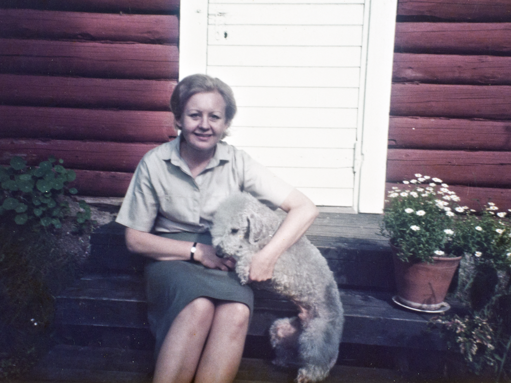 Syvärannan talonmiesperheen tytär Maija Tuomainen ja koira Valkoisen talon kivikellarin edustalla todennäköisesti 1980-luvulla.