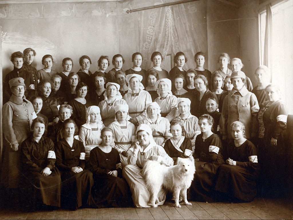 Turkulaislotilla on valokuvassa yllään joko oma siviilipuku, Turun lottien sininen puku tärkätyn valkoisen päähineen kanssa tai vuonna 1922 hyväksyttyä lottien sarkajakkupuku.